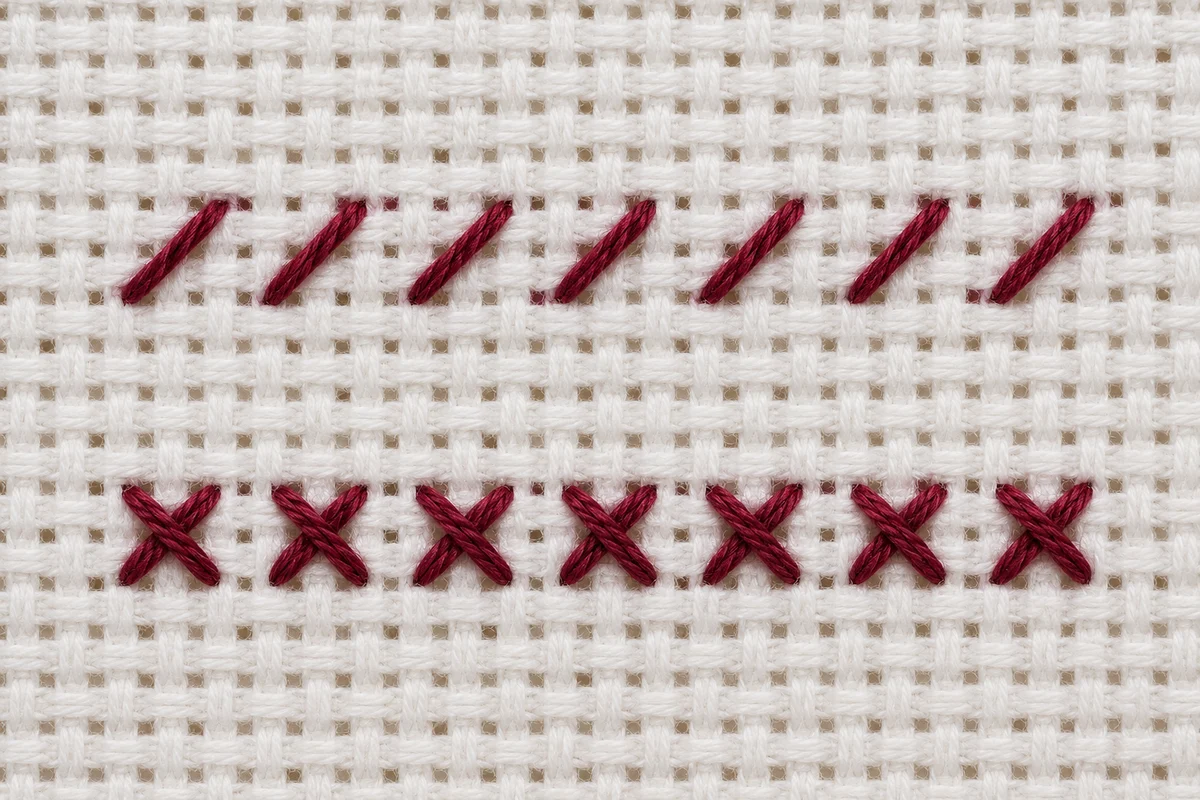 Macro view of burgundy diagonal half stitches and complete cross stitches on white Aida